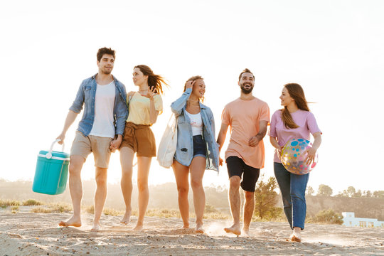 Image of young happy people smiling and walking together by seaside
