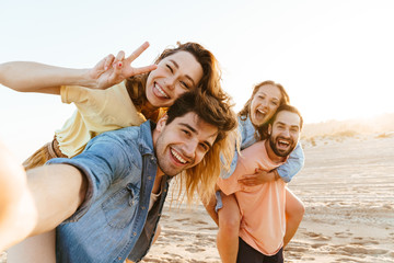 Image of young people smiling and taking selfie while walking on beach