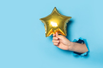 Male hand holding a golden balloon on a blue background.
