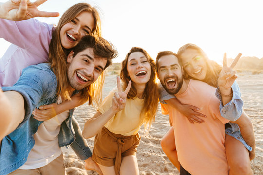 Image of young people smiling and gesturing peace sign by seaside