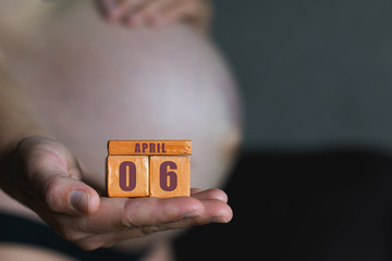 april 6th. Day 6 of month,planned date of birth. Month and day placed on wood calendar in pregnant womans hand. spring month, day of the year concept