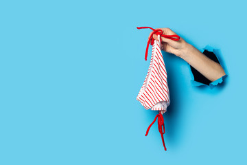 Woman's hand on a blue background holds white panties with red stripes.