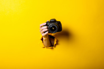Female hand holding a camera on a bright yellow background