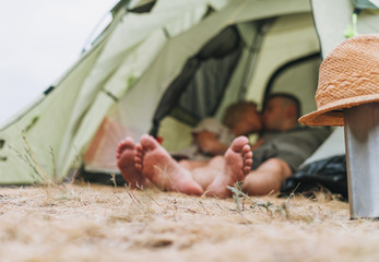 Happy young couple travelers in casual outfits kissing in tent. focus on straw hat. Local tourism, weekend trip