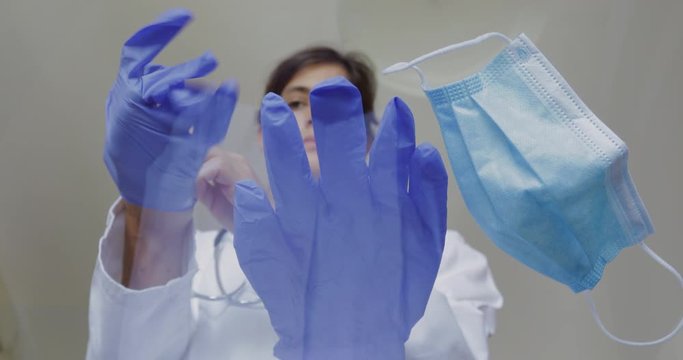 Female doctor or nurse is preparing to receive patients during an epidemic. She puts on a medical mask and disposable gloves. 