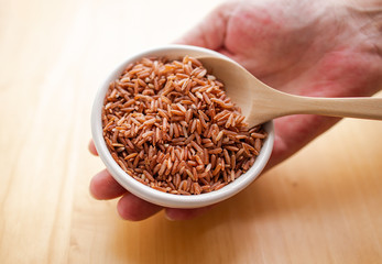 Closeup brown rice or red rice with wooden spoon and white ceramic bowl on wood table top. Healthy organic food concept.