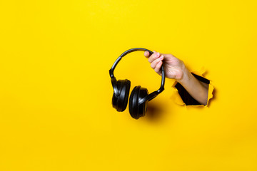 Female hand holding a black headphones on a bright yellow background
