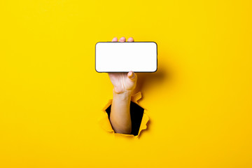 Female hand on a yellow background holding a phone horizontally.