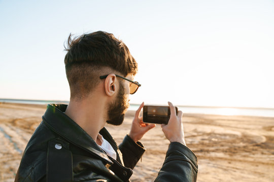 Back view of an stylish young bearded man taking picture