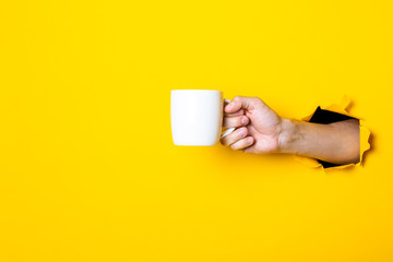 Man's hand holding a white cup on a bright yellow background