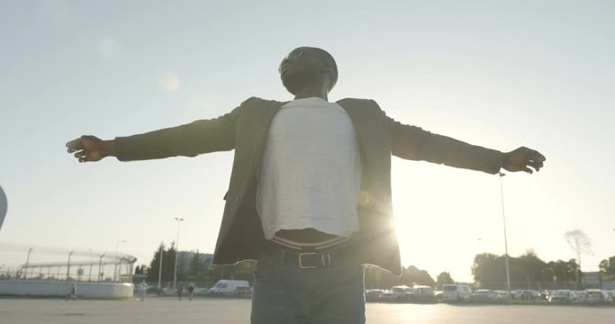 Half-length portrait of the calm attractive afro-american man in sunglasses raising hands up. he is stratching his body outdoor.