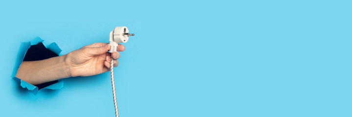 Female hand holding the plug on a bright blue background. Banner.