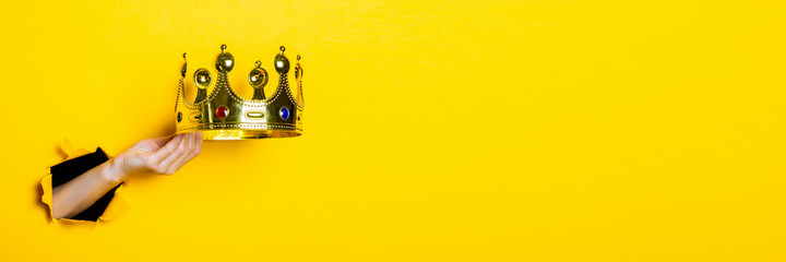 Female hand holds a gold crown on a bright yellow background. Banner