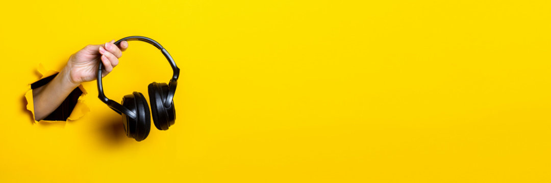 Female hand holding headphones on a bright yellow background. Banner.