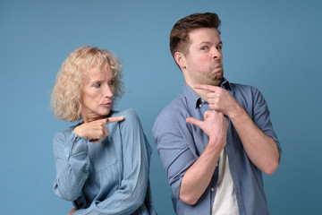 Woman and man pointing fingers at each other, blaming each other for problems, isolated on blue background. Negative emotion facial expression feelings