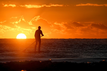 Fototapeta premium A silhouette of a stand Up Paddle Border on the water as the sun rises on the horizon.