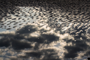 abstract clouds reflected in beach pond water during sunrise