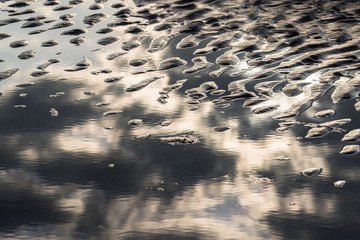 abstract clouds reflected in beach pond water during sunrise