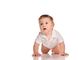 Calm little baby boy in a white shirt crawls on all fours on a white background.