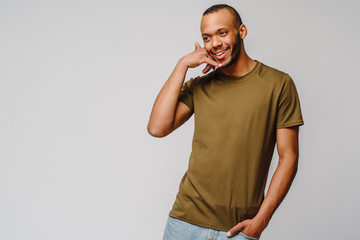 Handsome young African American man showing a call me sign and smiling while standing isolated on grey background