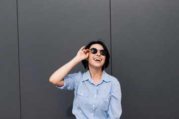 Smiling attractive girl of caucasian ethnicity posing in sunglasses and in a blue shirt, outdoors