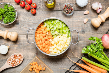 Top view of a saucepan and a variety of fresh raw vegetable ingredients for making vegetable soup.