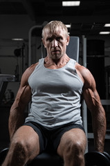 Fototapeta na wymiar Muscular adult brutal man with dumbbells pumps biceps in the gym. Portrait of caucasian authentic bodybuilder doing workout exercises