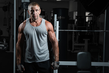 Fototapeta na wymiar Close-up portrait of adult Caucasian brutal bodybuilder with serious face and muscular body posing in the gym