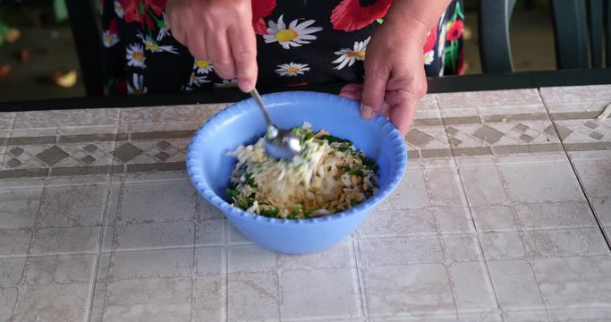 A woman at a street table in the garden mixes a filling of cheese, eggs and herbs to make pies.