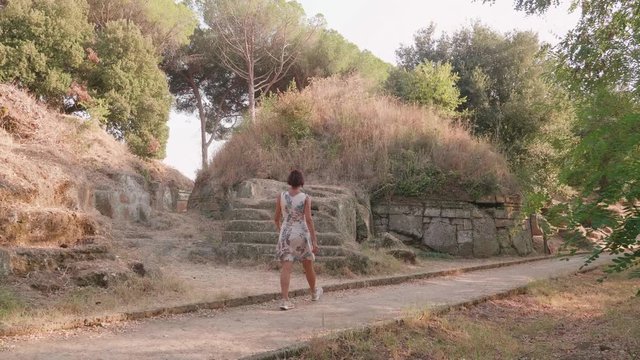 A woman exploring exterior of old etruscan tumulus. Archeological site, history tourism concept. Necropolis site. Cerveteri, Italy 