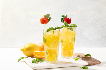 Citrus lemonade or mojito cocktail with lemon and orange and basil. Cold beverage or drink with ice on marble cutting board