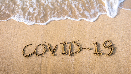 Covid19 written on the sand of shore beach with incoming wave washing