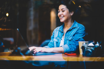 Cheerful skilled freelancer laughing while watching interesting video in website on laptop during...