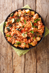 Spicy rice with chicken, zucchini and mushrooms in tomato sauce close-up in a frying pan on the table. vertical top view from above