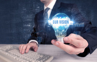 Businessman holding a light bulb with OUR VISION inscription, new business concept