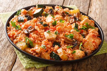 One pot of rice with chicken, zucchini and mushrooms, tomatoes, herbs close-up in a frying pan on the table. horizontal