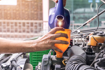Auto mechanic is filling up the car's engine oil inside the auto repair center, the auto industry and garage ideas.
