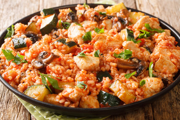Delicious rice with chicken, zucchini and mushrooms, tomatoes, herbs close-up in a frying pan on the table. horizontal