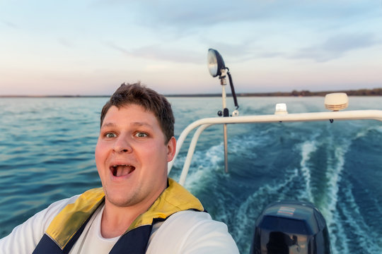 Young adult happy caucasian excited man portrait enjoy having fun driving fast motorboat on pond water surface at sunset evening time. Male person sailing fishing on speedboat by lake in morning