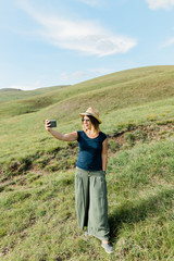 Young woman taking a selfie on hillside meadow in summertime