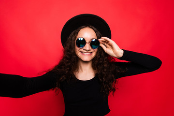 Portrait of young girl wearing hat showing peace gesture isolated over red background