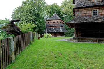 Fototapeta na wymiar Hrebenne, Poland - July 23, 2020: Wooden bell tower and part of church architecture built in year 1700. Cut tree behind wooden fence.