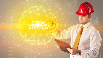 Handsome businessman with helmet drawing SOCIAL STRATEGY inscription, social construction concept