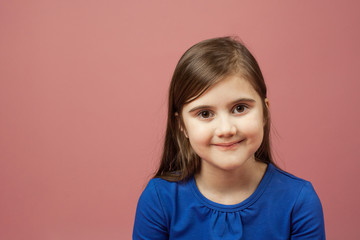 Fototapeta premium Funny smiling little girl on the pink background. Blue dress, copy space.