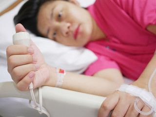 Focus at hand of sickness woman hold pressing emergency call remote button to call nurse and doctor for help, laying on the hospital patient bed, healthcare and medical concept.