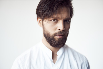 portrait photo of a handsome bearded man with brown hair and eyes on white background, he is dressed in a white linen shirt and looks at the camera