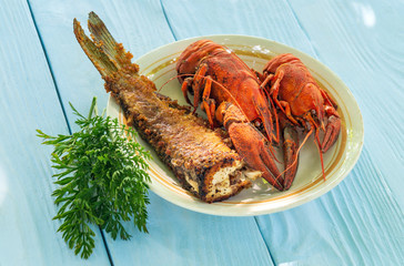 Boiled crayfish and fried fish on plate with a bunch of dill before dinner