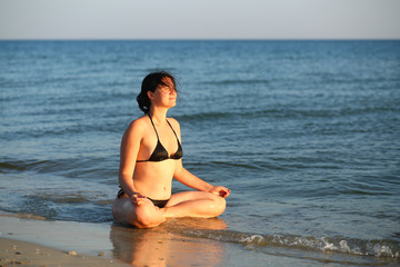 Fototapeta na wymiar 35 year old caucasian woman doing yoga at the sunset sea shore. Body positive