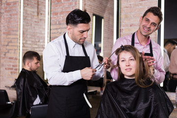 Attractive long-haired brunette getting haircutting from two professional hairstylists in salon