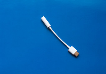 An adapter for a USB to 3.5mm type c headphone cable on a smartphone. Close up white cable and 3.5mm audio cable on blue background